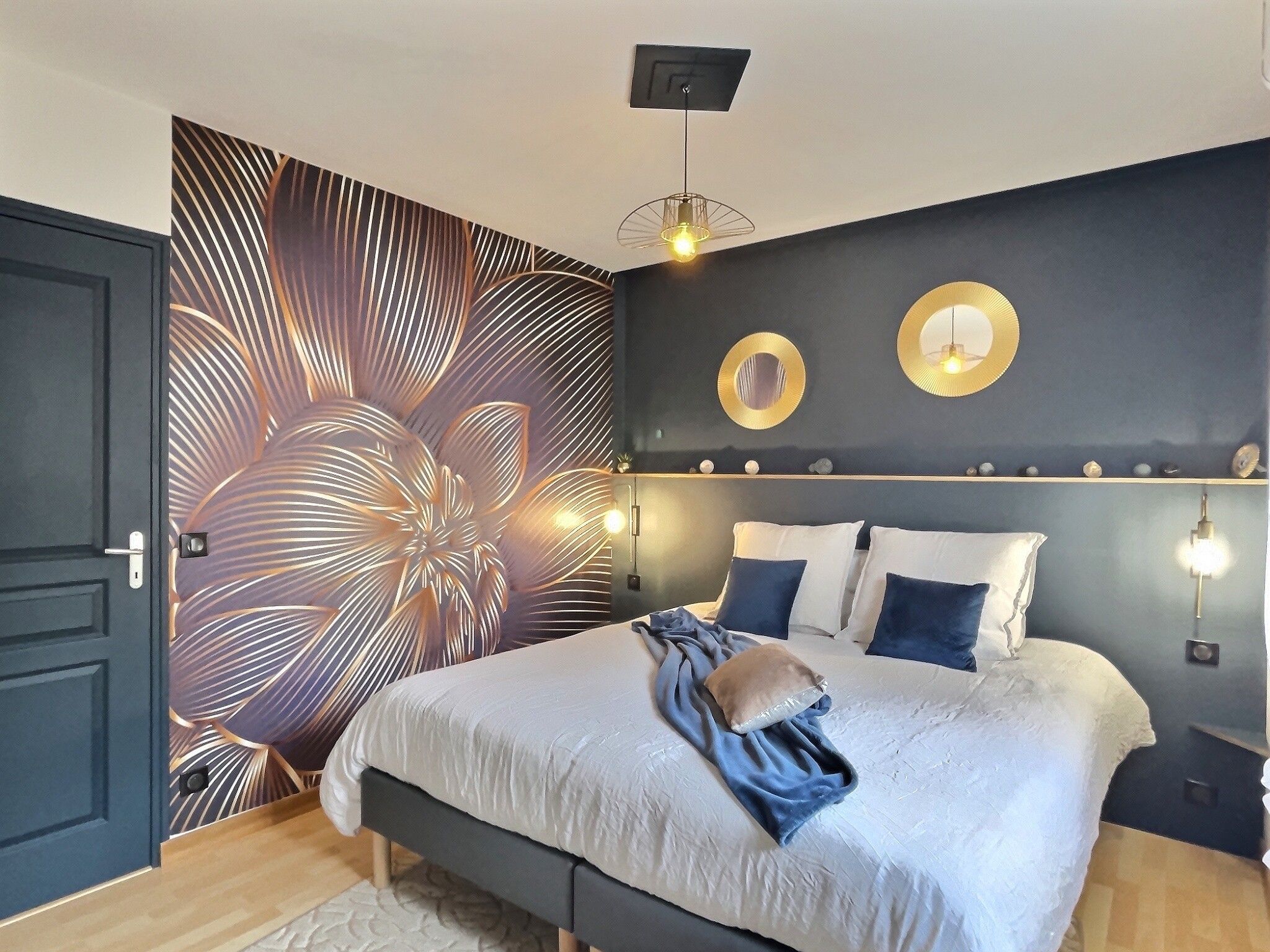 Une chambre à coucher avec un lit, des lampes de chevet, un mur orné d’un miroir rond et une porte.
