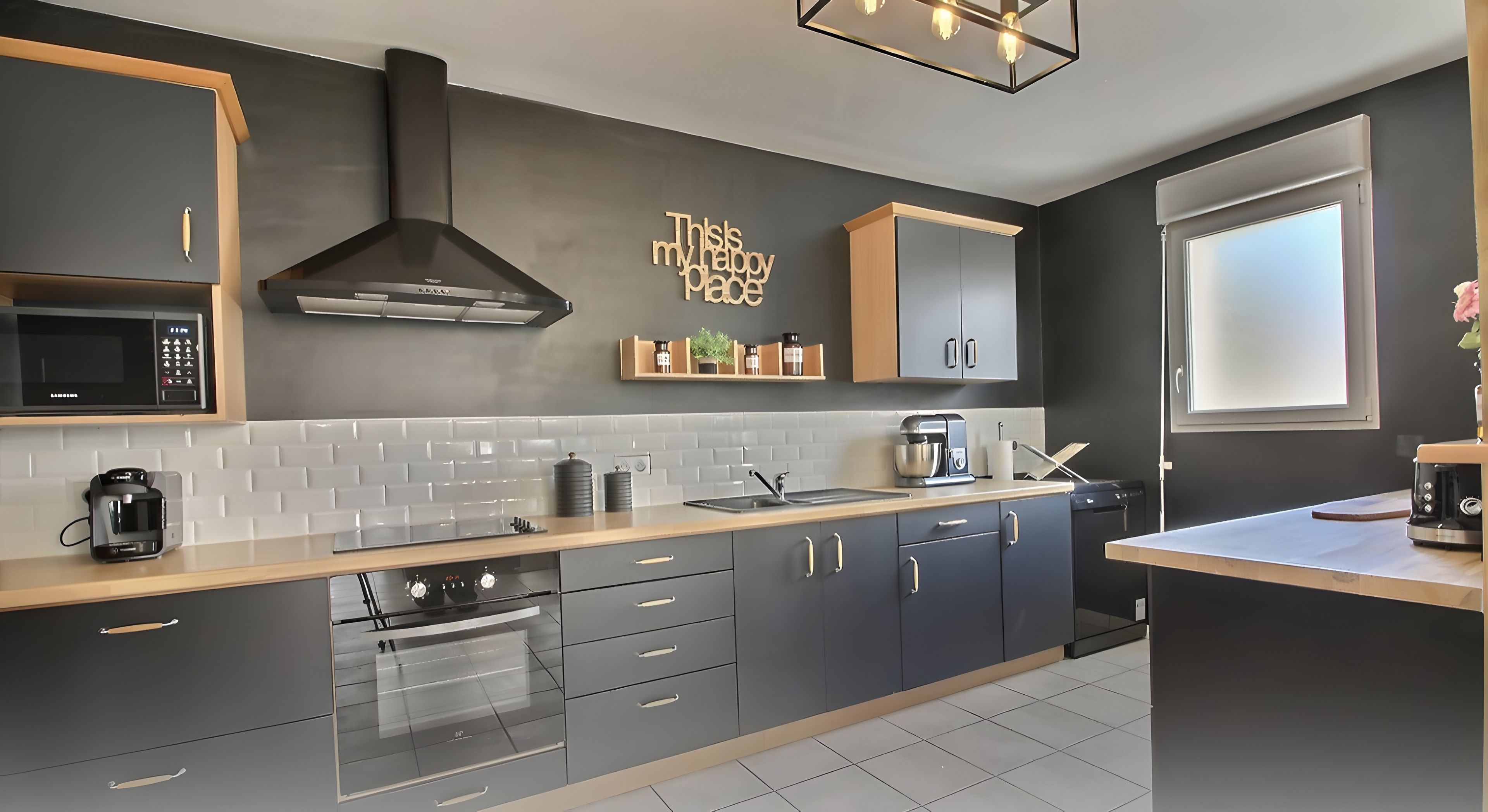 Una cucina moderna con forno a microonde, forno e lavandino. Un cartello decorativo è appeso al muro e una finestra lascia entrare luce naturale.