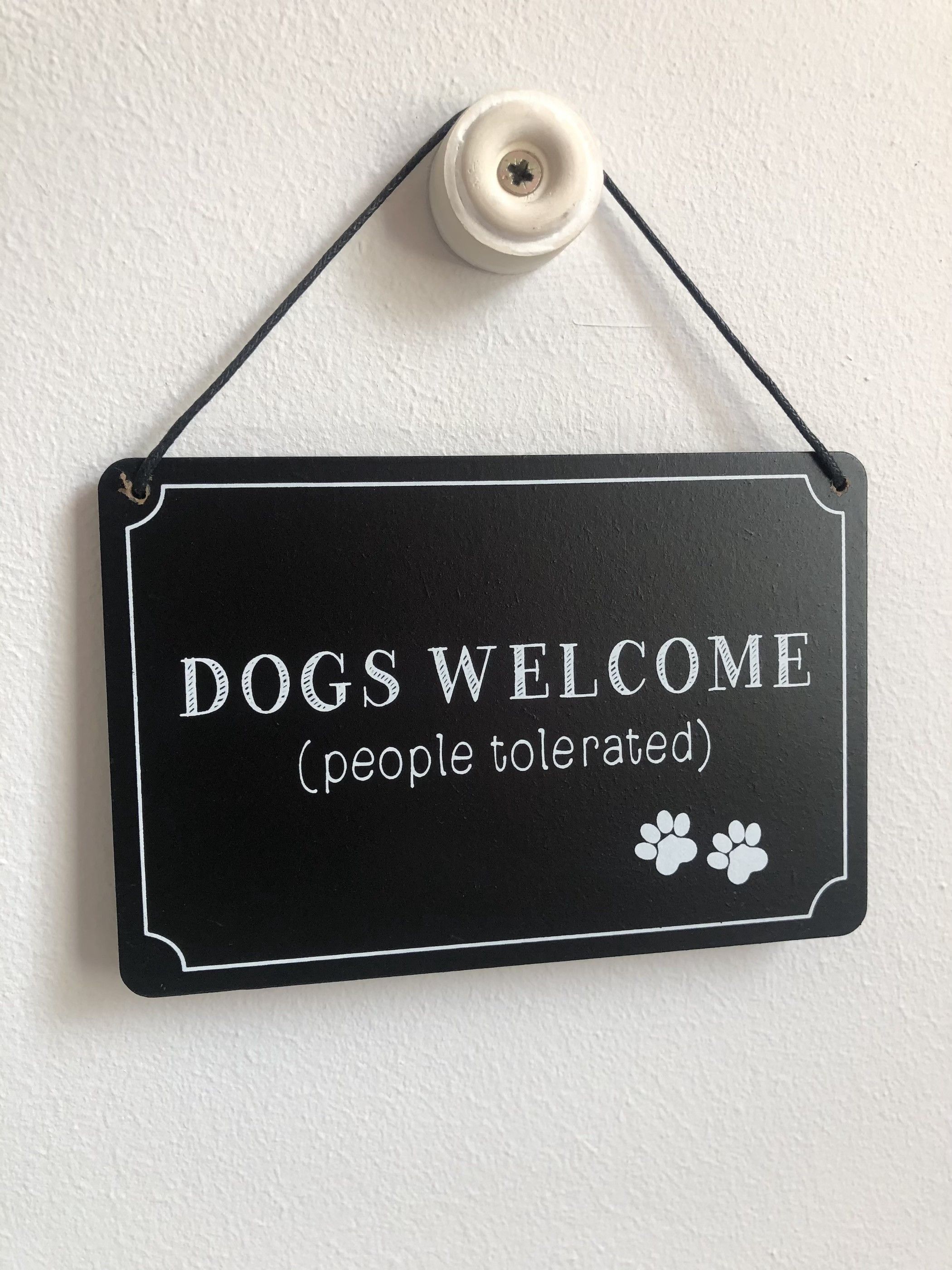 A black sign with white lettering that reads 'Dogs Welcome (people tolerated)' and two white paw prints.