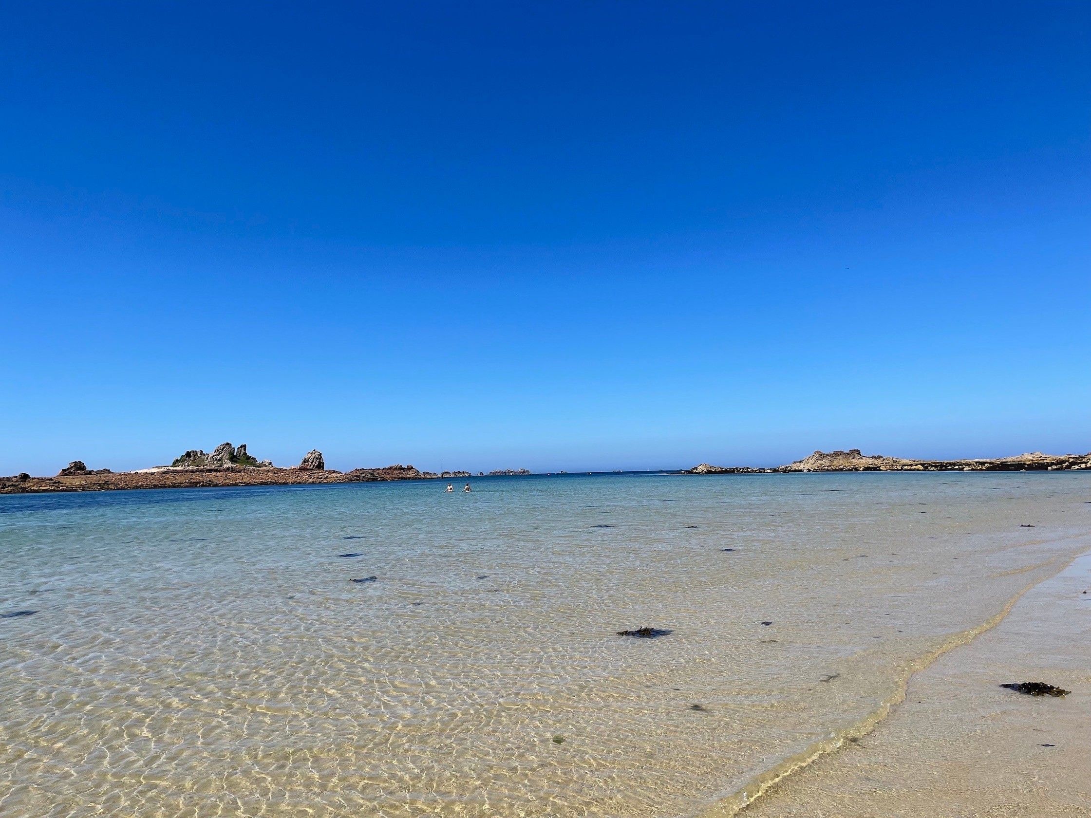 Una spiaggia con acque limpide e poco profonde, affioramenti rocciosi e cielo sereno.