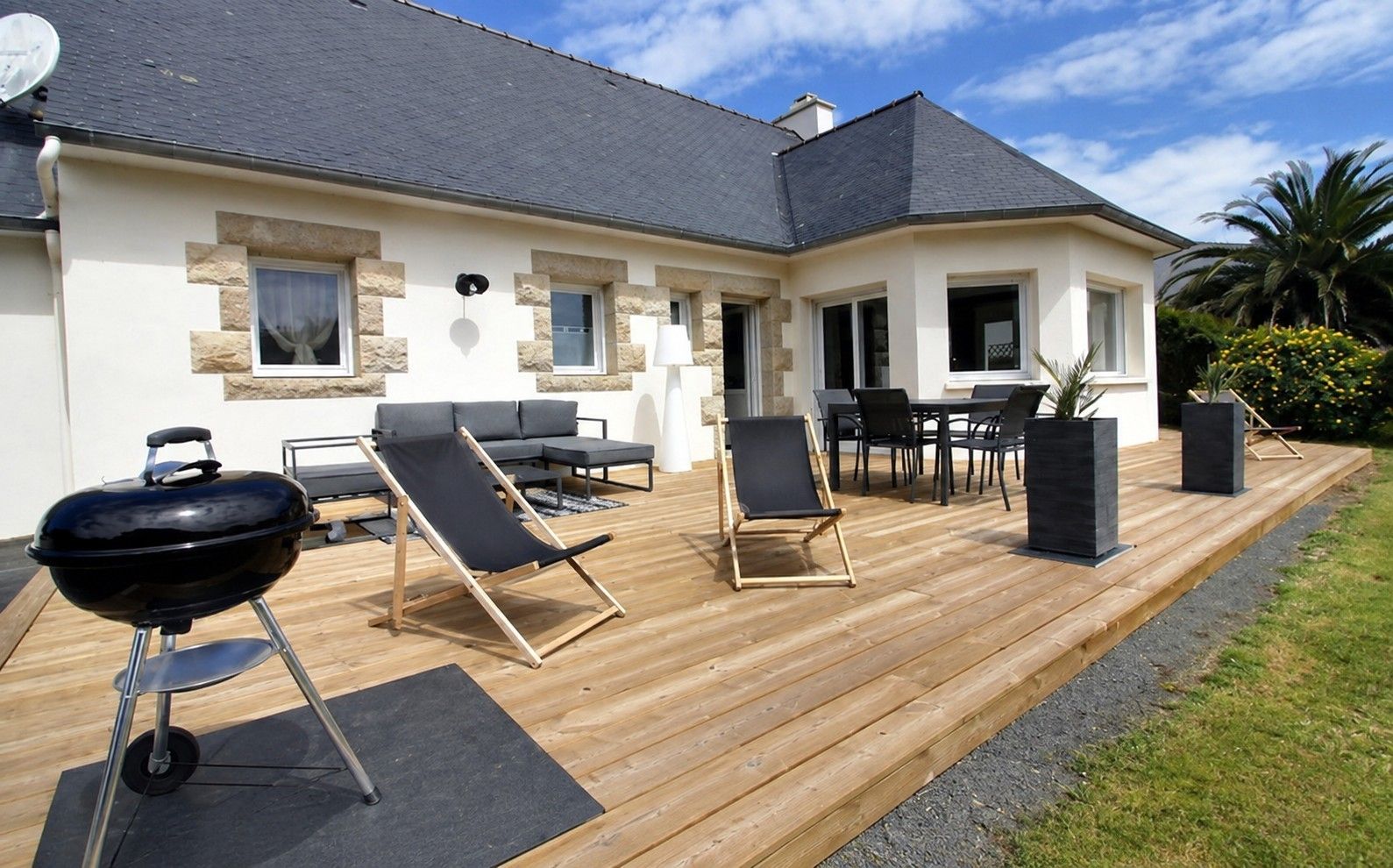 Une maison avec une terrasse, du mobilier d’extérieur et un barbecue.