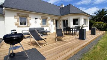 Une maison avec une terrasse, du mobilier d’extérieur et un barbecue.