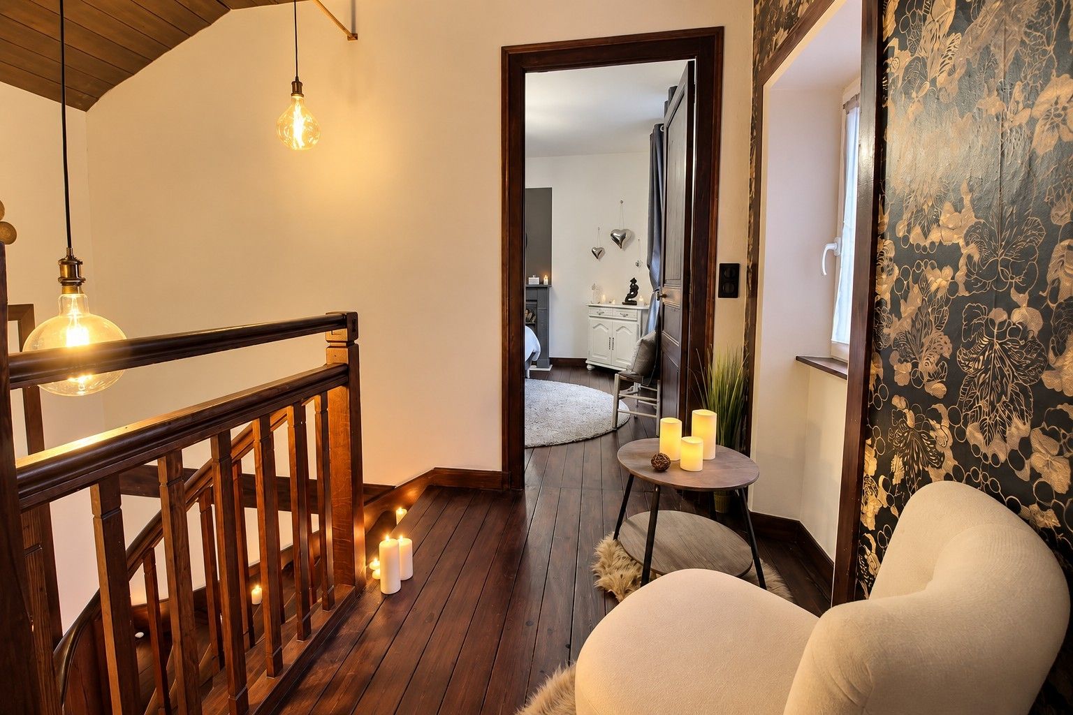 A staircase with wooden railings and a light fixture, leading to a room with a round table and candles.