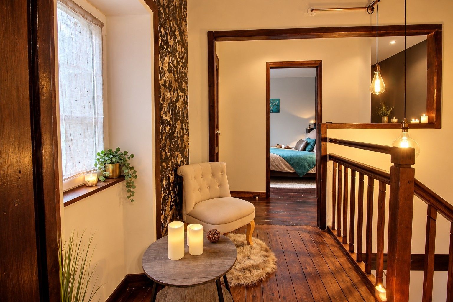 A cozy hallway with a chair, a round table with candles, and a staircase leading to a bedroom.