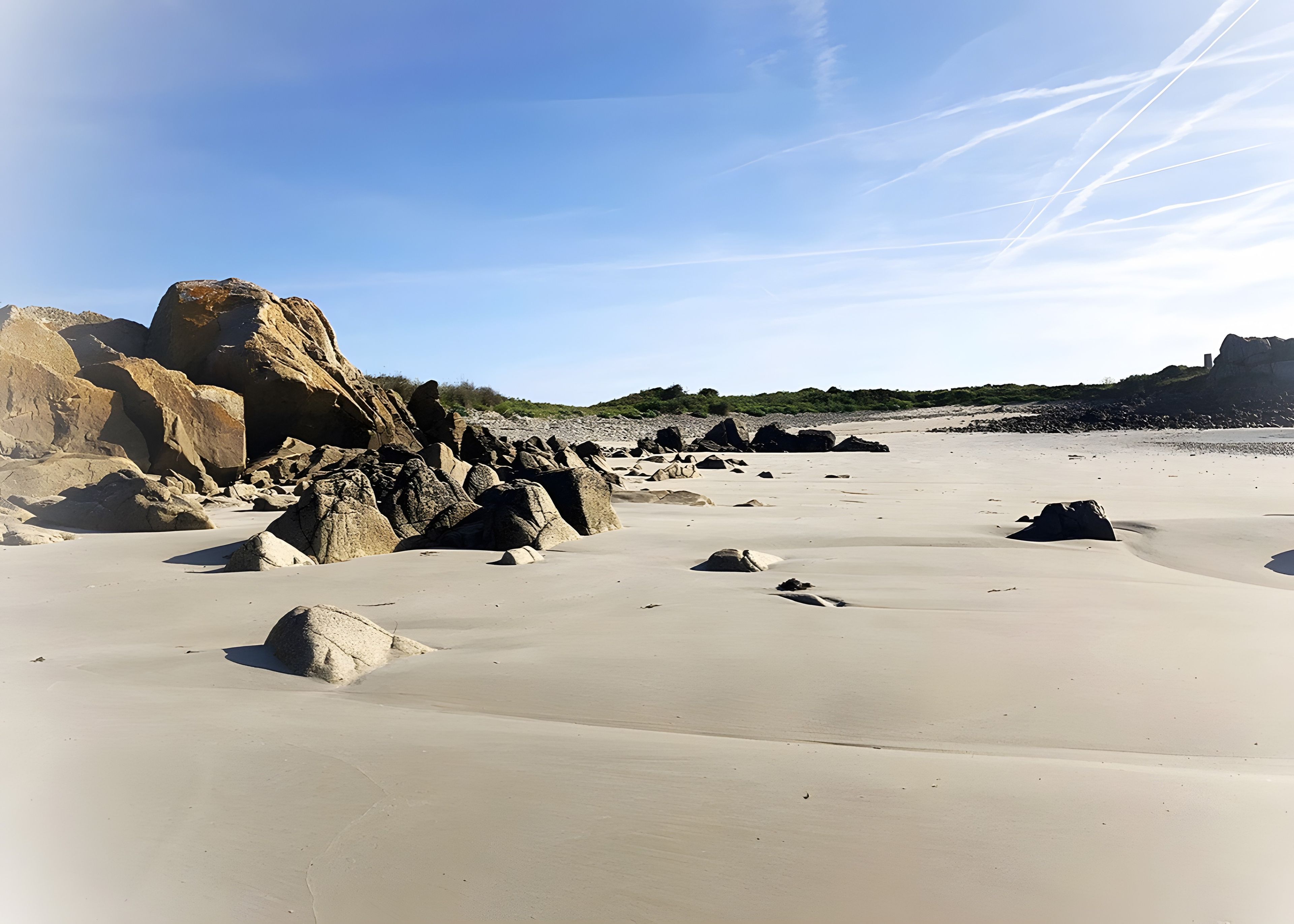 Ein Strand mit großen Felsen und blauem Himmel.