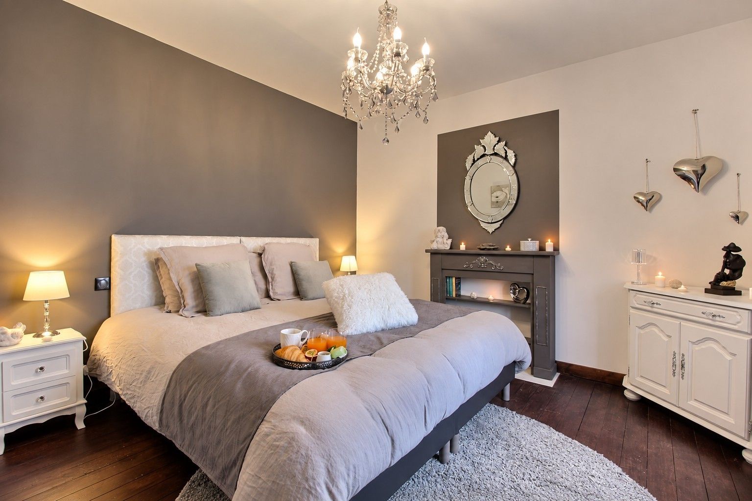 A bedroom with a bed, bedside tables, a chandelier, a fireplace, and decorative items.