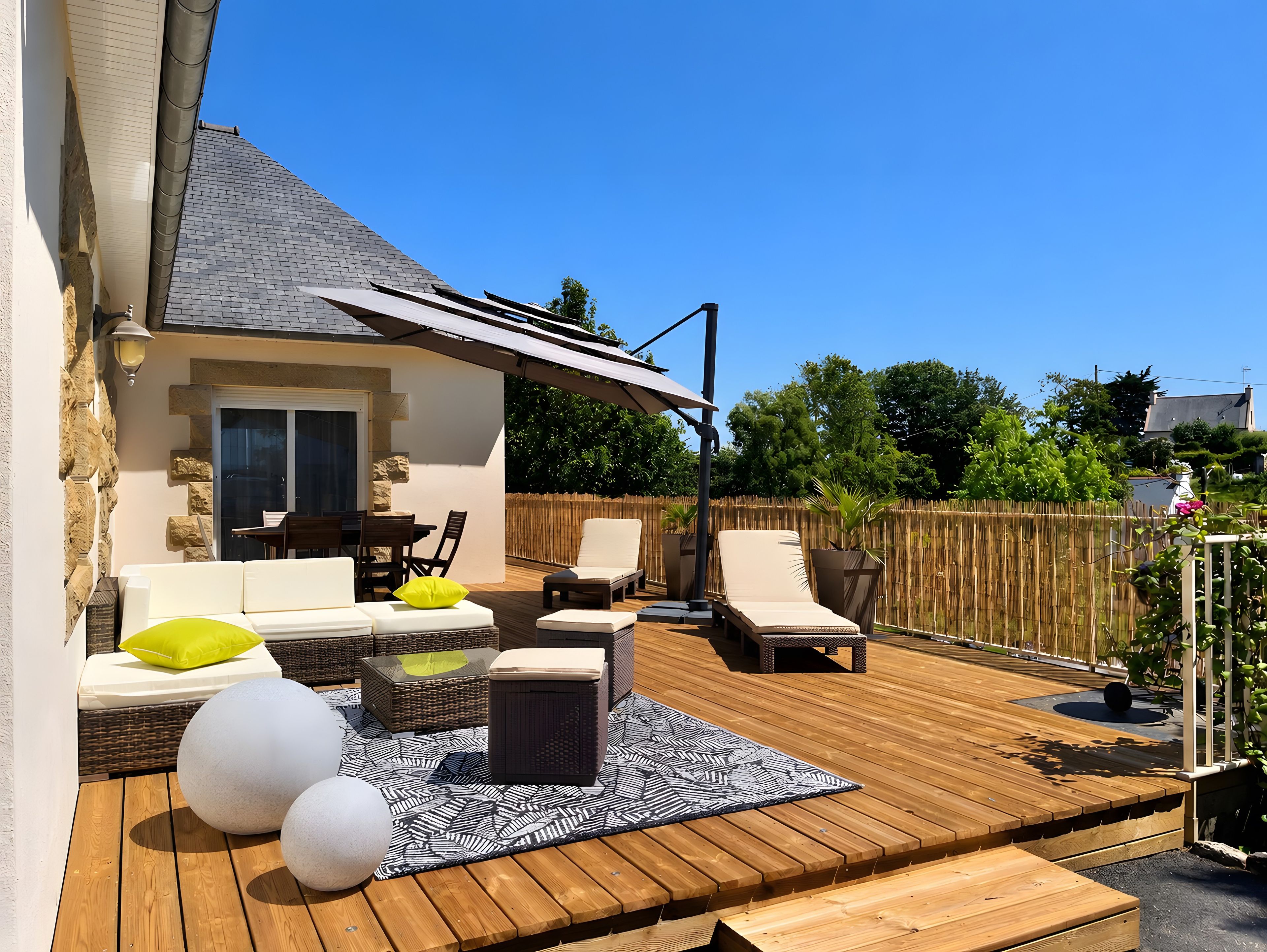 A wooden deck with outdoor furniture, a covered patio area, and a stone wall.