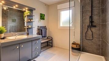 A modern bathroom with a large mirror, a sink, a shower, and a window.