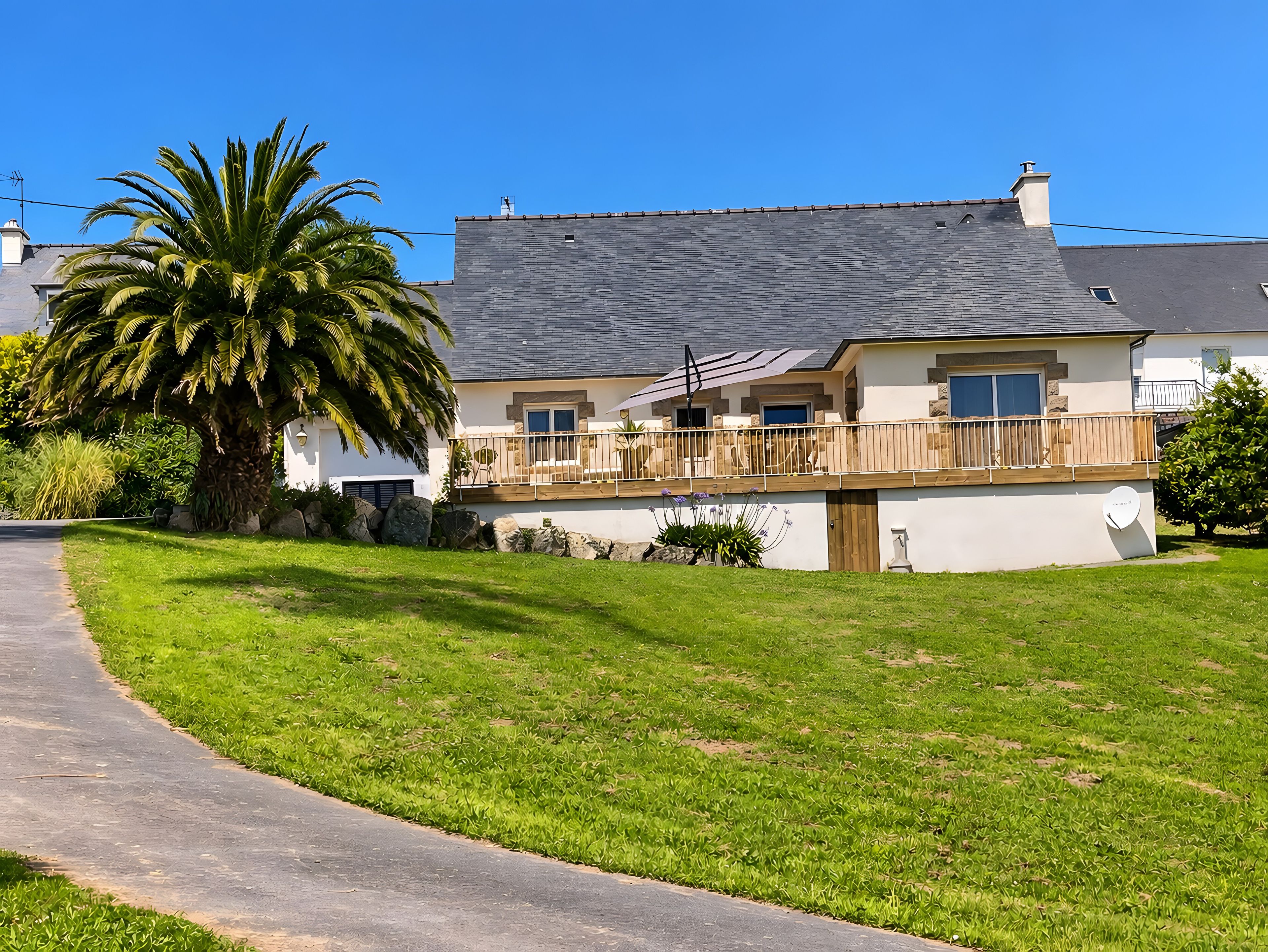 Une maison à deux étages avec un balcon, une allée pavée et un grand palmier.