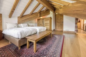 Une chambre avec un plafond en bois, un grand lit avec une literie blanche, un banc et un tapis à motifs.