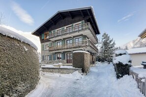 Ein mehrstöckiges Chalet mit Balkon, Steinfundament und verschneiter Umgebung.