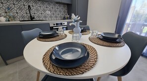 Et spisebord dækket med tallerkener, skåle og en vase, i et moderne køkken med mønstret bagvæg og udsigt til det fri.