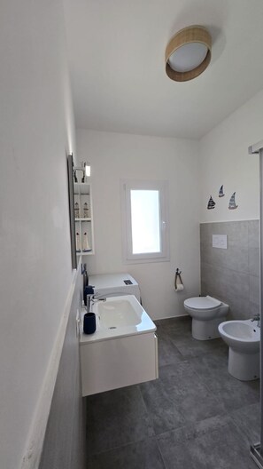 Ein modernes Badezimmer mit einem großen Waschbecken, einer Toilette und einem Bidet. Ein Fenster bietet einen Ausblick nach draußen.