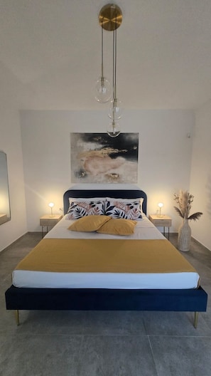 Ein modernes Schlafzimmer mit einem großen Bett, einem an der Wand befestigten abstrakten Gemälde und einer hängenden Leuchte.