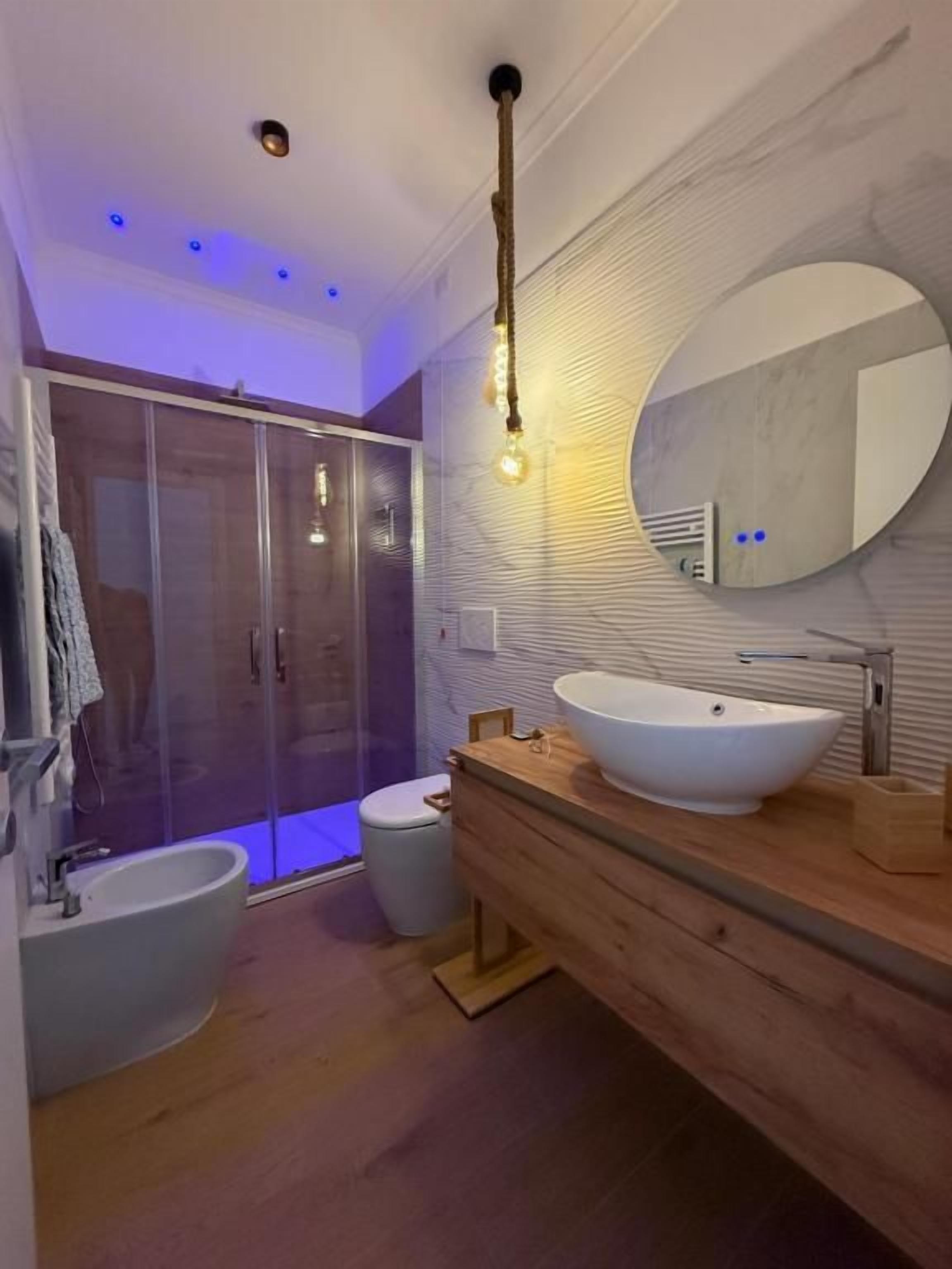 Een moderne badkamer met een grote spiegel, een vrijstaand badkamermeubel, een bidet en een inloopdouche.