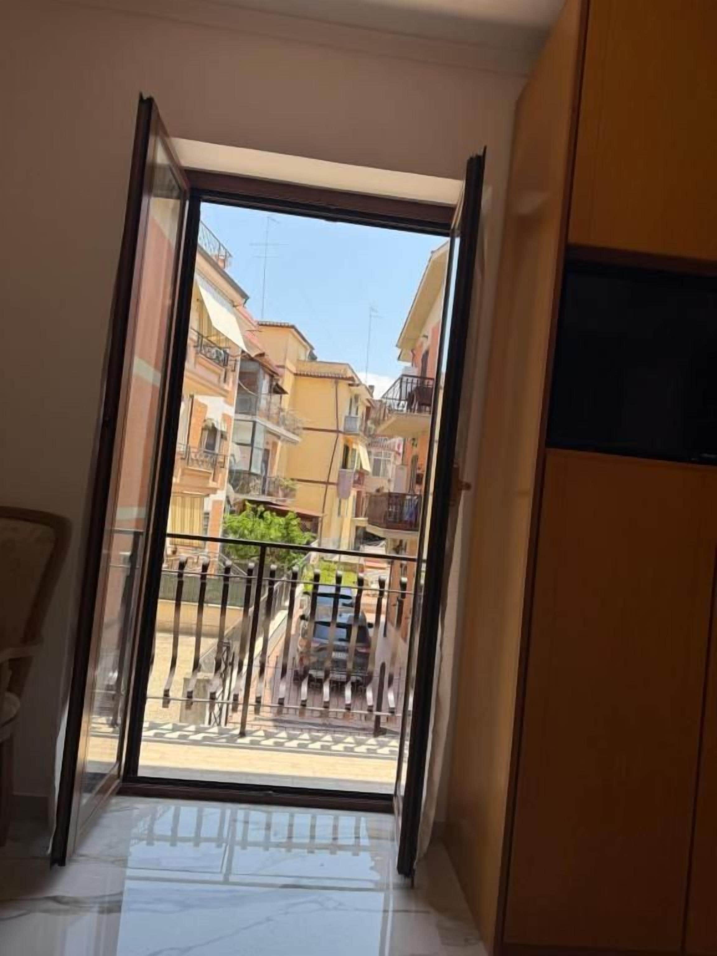 A room with a sliding glass door leading to a balcony with a view of a street and buildings.