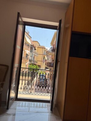 A room with a sliding glass door leading to a balcony with a view of a street and buildings.