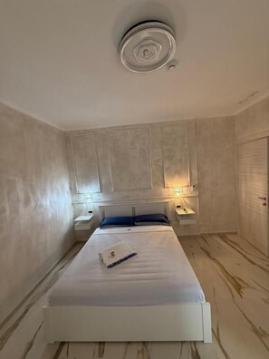 A bedroom with a bed, bedside tables, and wall-mounted lighting.