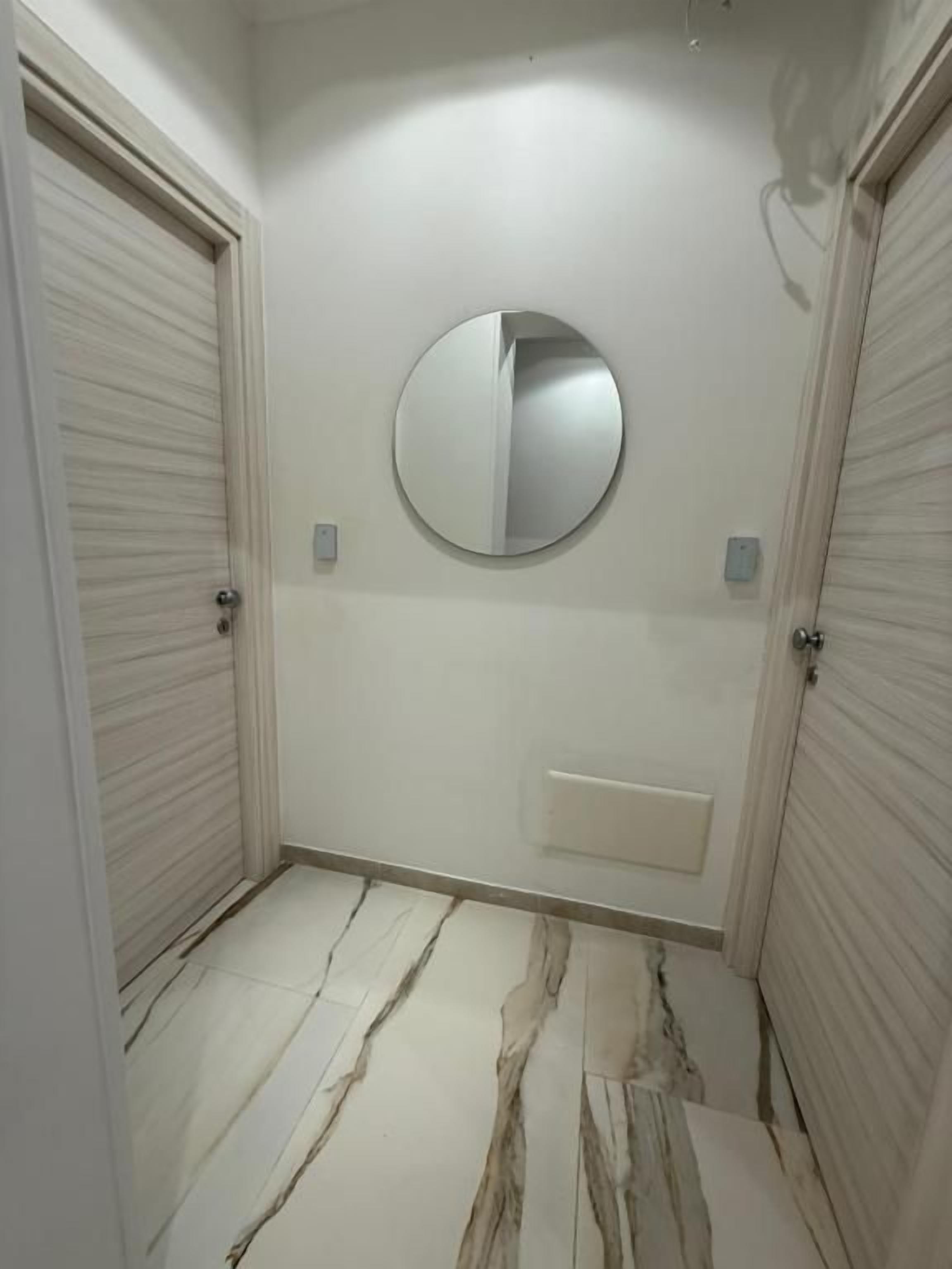 A hallway with two closed doors, a round mirror on the wall, and a marble-patterned floor.