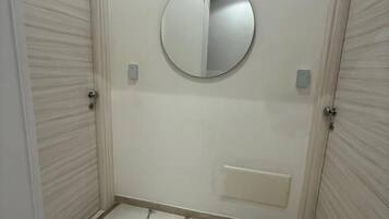 A hallway with two closed doors, a round mirror on the wall, and a marble-patterned floor.