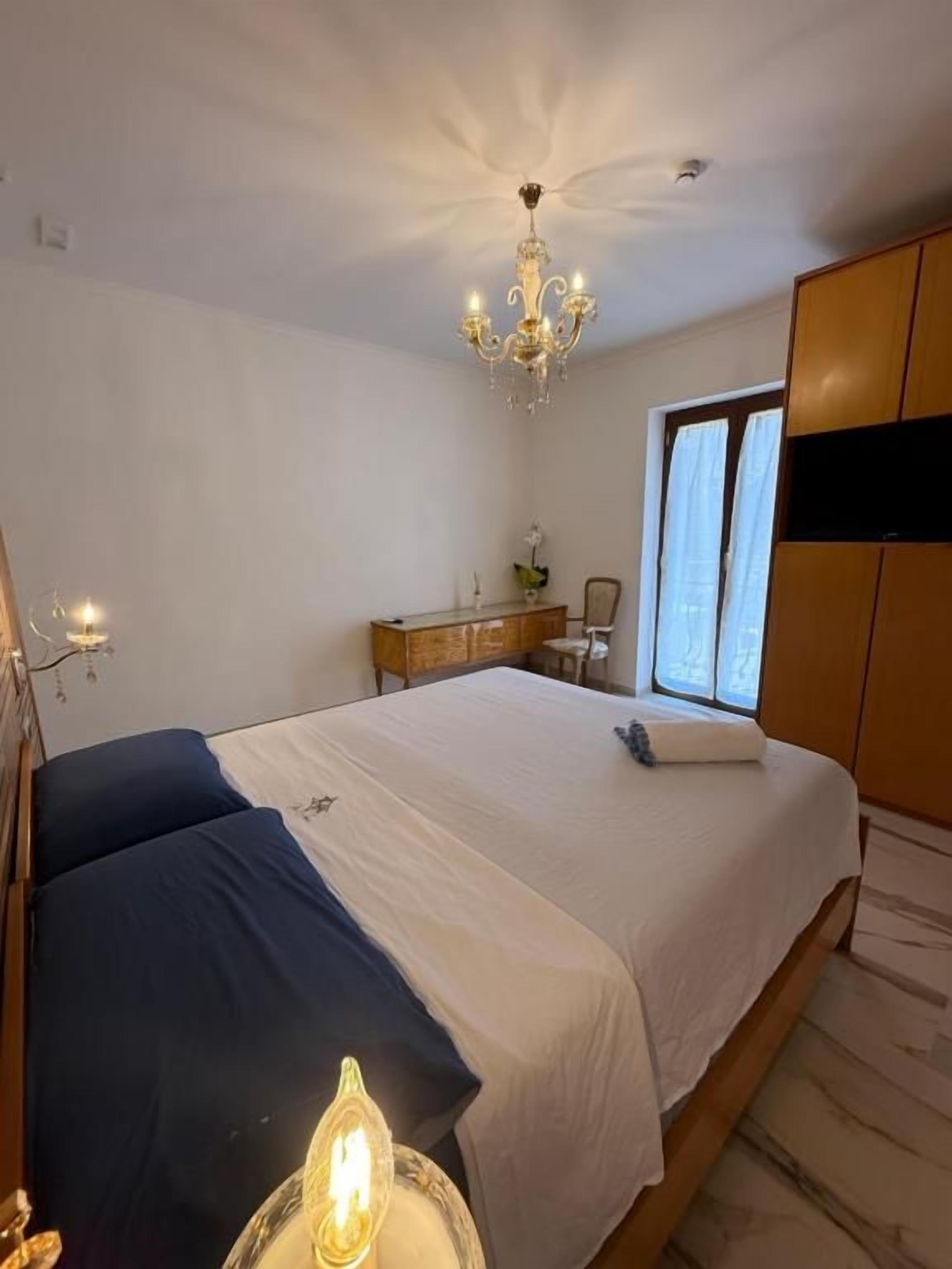 A bedroom with a bed, a chandelier, a wardrobe, and a window.