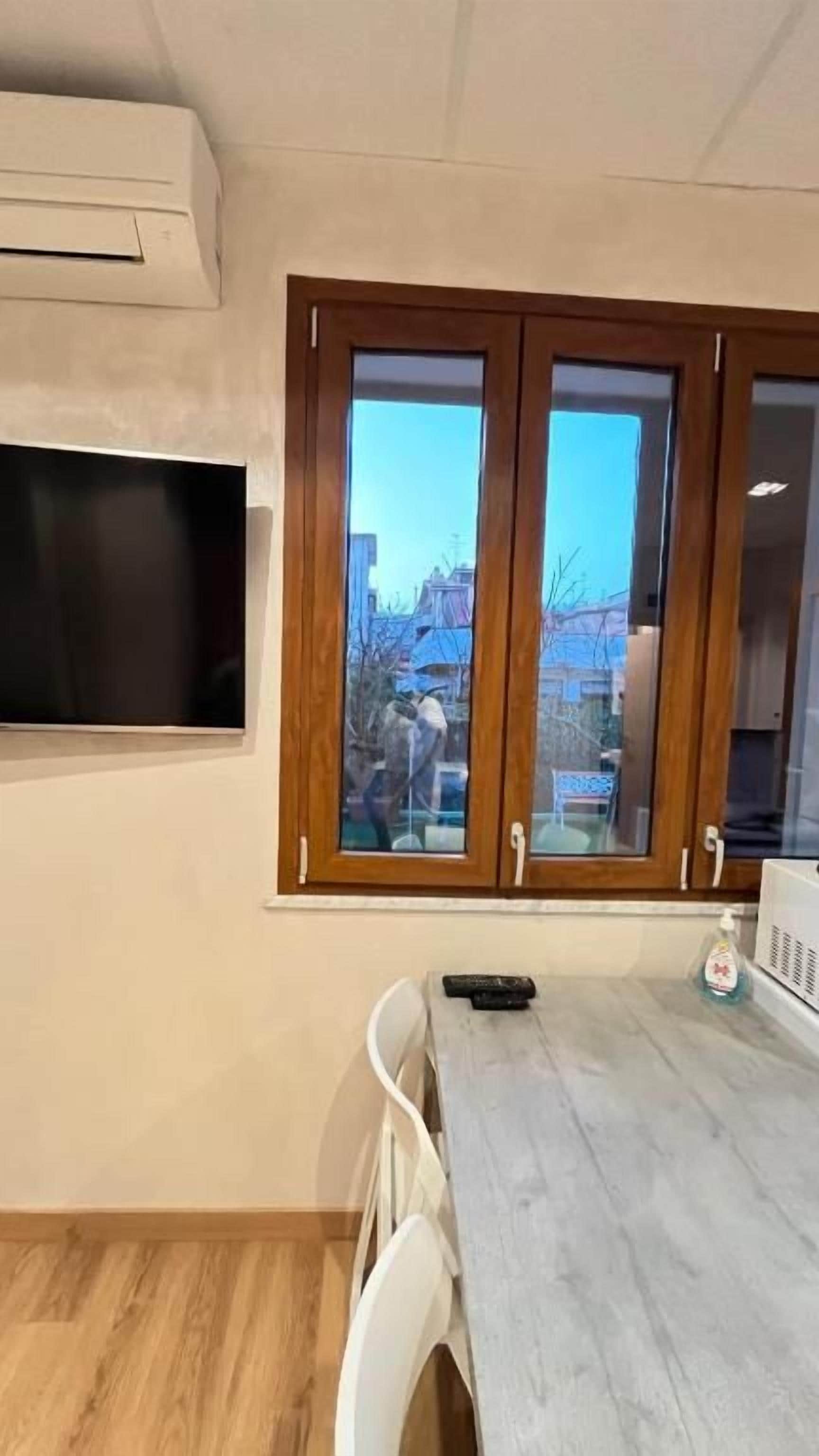 Una stanza con un armadio in legno, un televisore a parete, un tavolo con sedie e una finestra vista esterna.