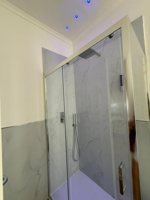 Ducha con cerramiento de vidrio, pared con azulejos de mármol y ducha a la vista.