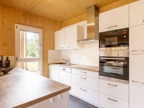 A modern kitchen with white cabinetry, stainless steel appliances, and a wooden ceiling. - One-bedroom Cabin (Sankt Georgen am Kreischberg)