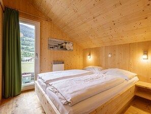 A wooden cabin room with two beds, a window with curtains, a wall-mounted light, and a painting. - One-bedroom Cabin (Sankt Georgen am Kreischberg)
