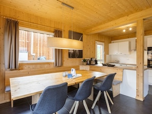 A wooden interior with a dining area, kitchen, and a window with curtains. - One-bedroom Cabin (Sankt Georgen am Kreischberg)