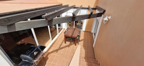 Un patio couvert avec une table et des chaises en bois, un barbecue et une plante en pot.