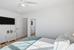 Ein Schlafzimmer mit Bett, Kommode, Wandfernseher und Deckenventilator.