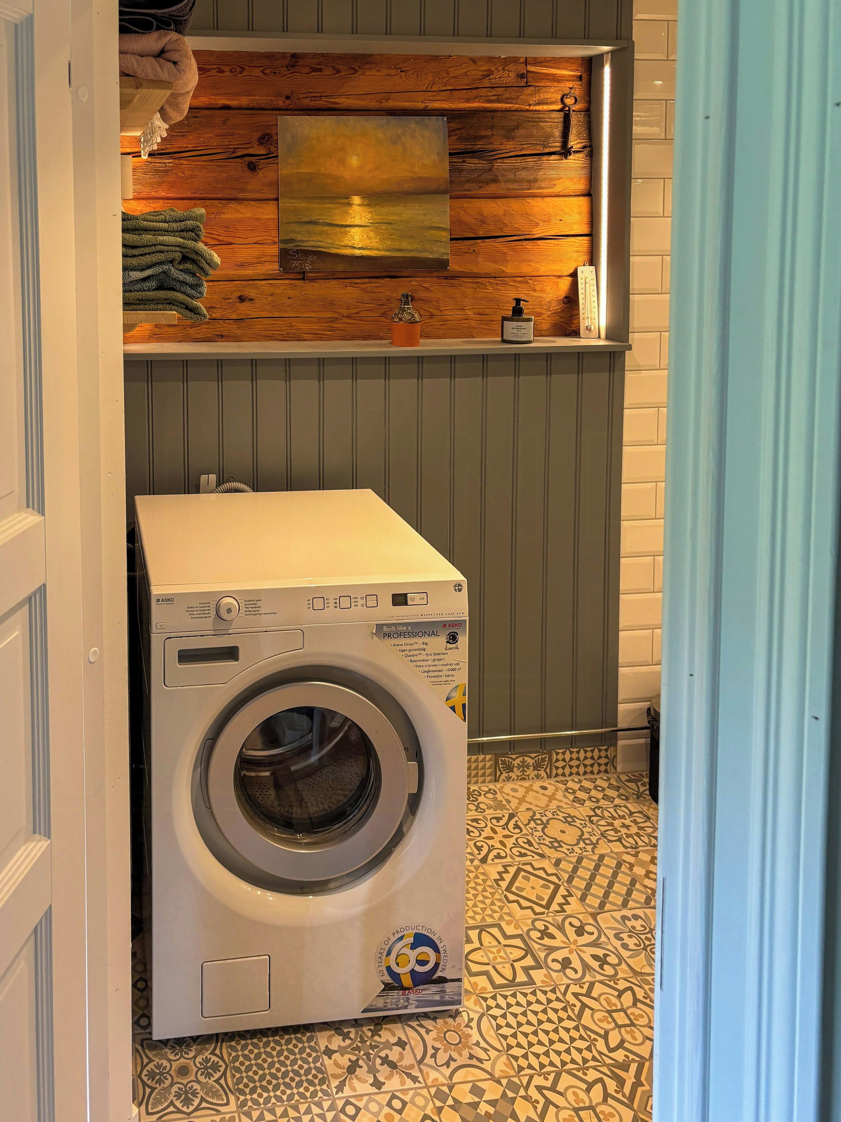 Une petite buanderie équipée d’un lave-linge, agrémentée de décorations murales en bois et dotée d’un carrelage au motif original.