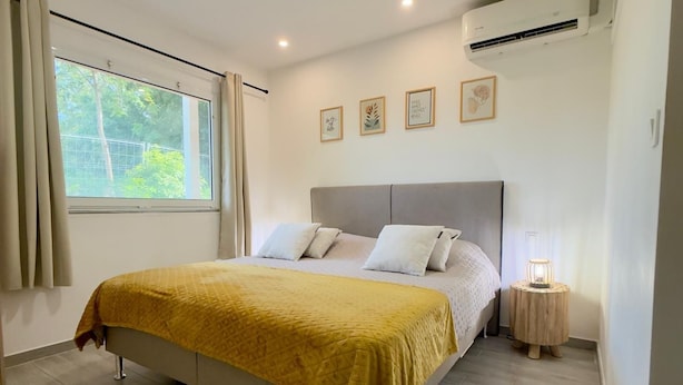 Ein Schlafzimmer mit einem Bett, einem Fenster mit Vorhängen, einer Klimaanlage und einer Nachttischlampe.
