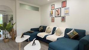 Ein modernes Wohnzimmer mit einem Ecksofa, zwei weißen Couchtischen und dekorativen Kissen.