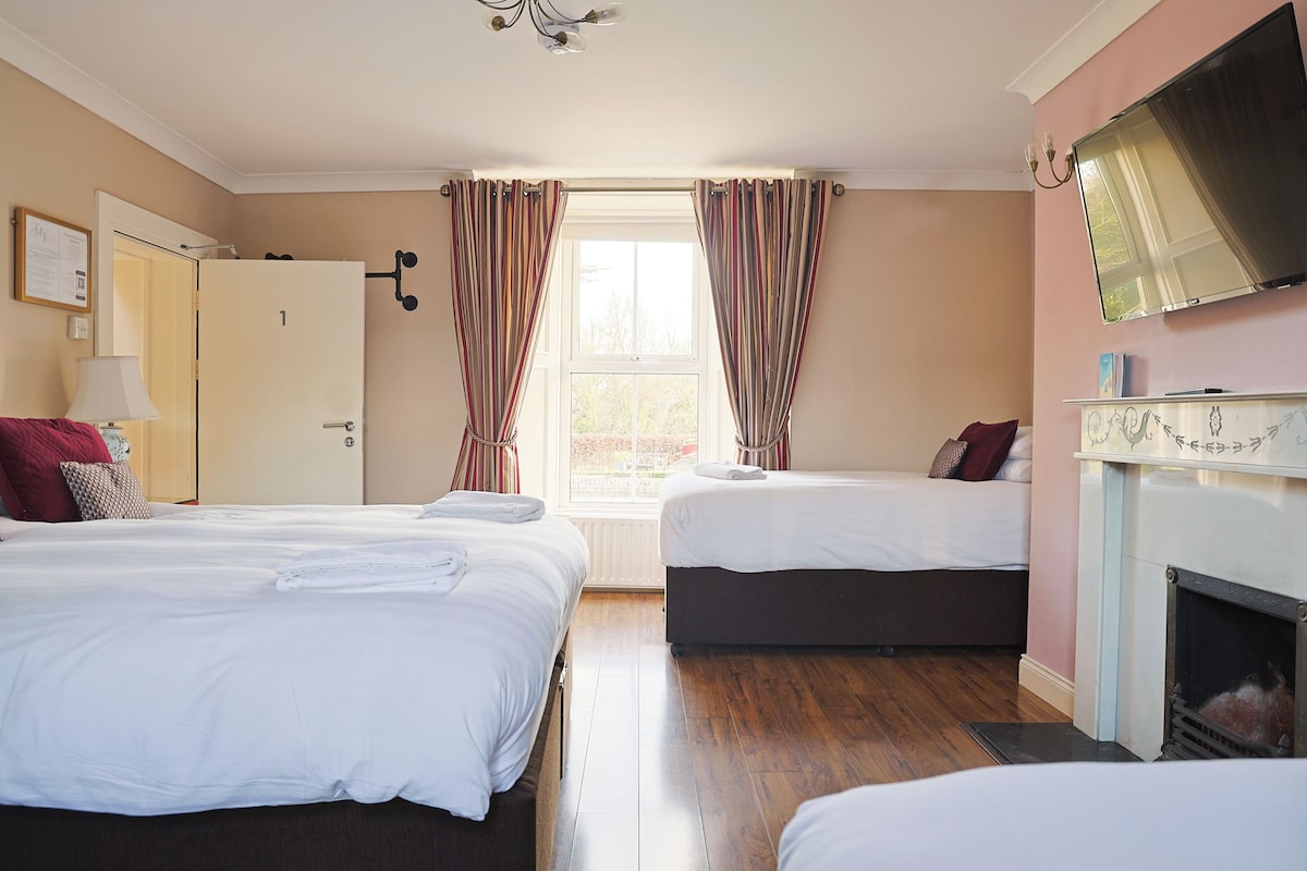A hotel room with two beds, a TV, a fireplace, and a window with curtains.