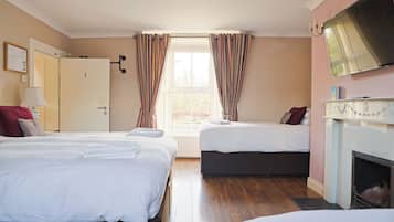 Ett hotellrum med två sängar, en TV, en öppen spis och ett fönster med gardiner.
