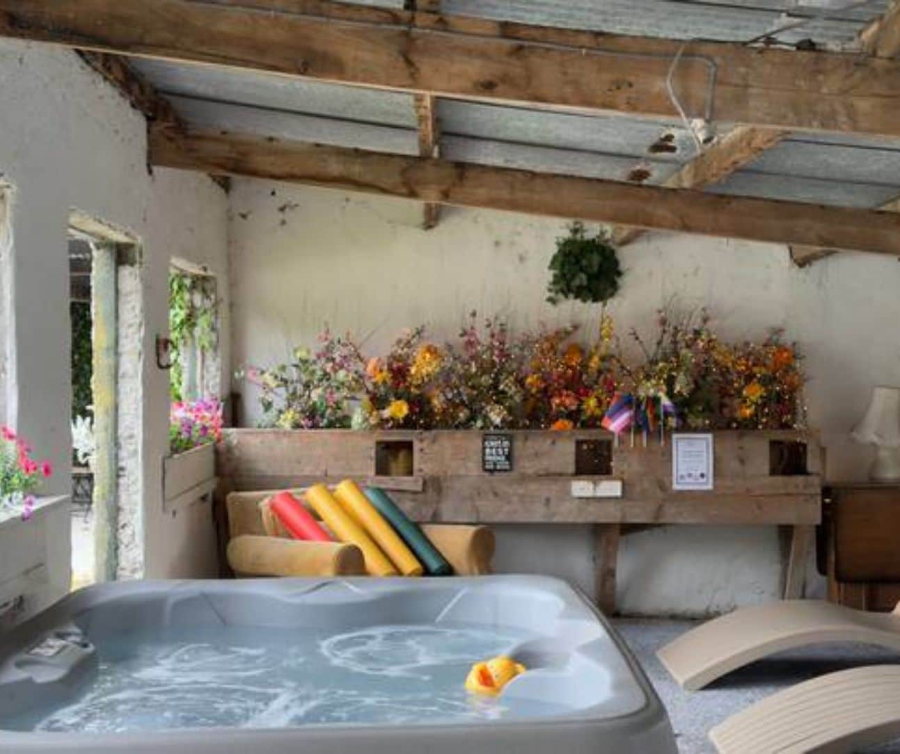 Una habitación con bañera de hidromasaje, vigas de madera y una pared decorada con flores.