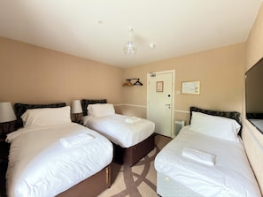 A hotel room with three beds, a door, a coat rack, and a mirror. - Fitz Of Inch - Guest House Rooms (Stradbally)