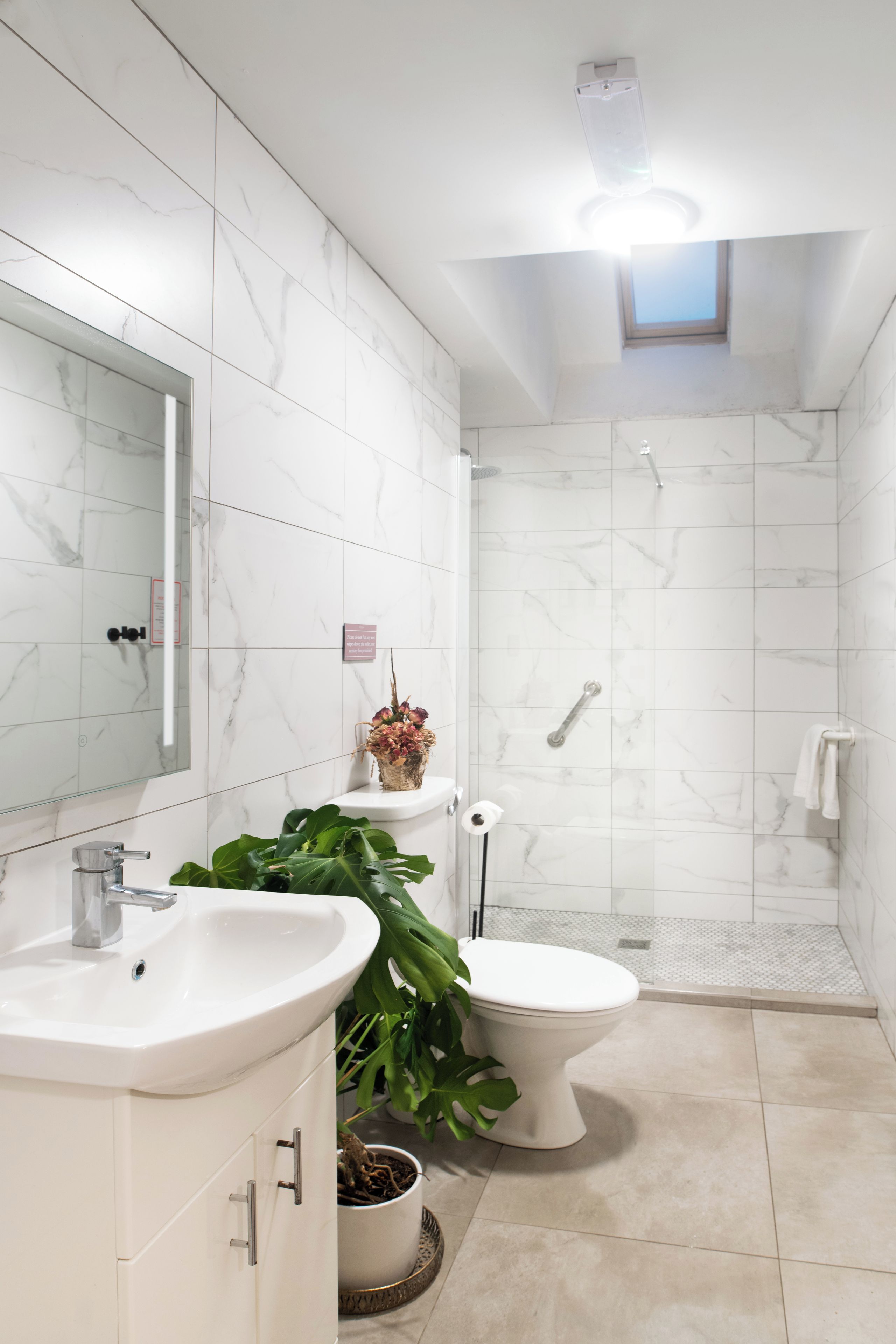A modern bathroom with a white marble wall, a large mirror, a sink, a toilet, and a shower area.