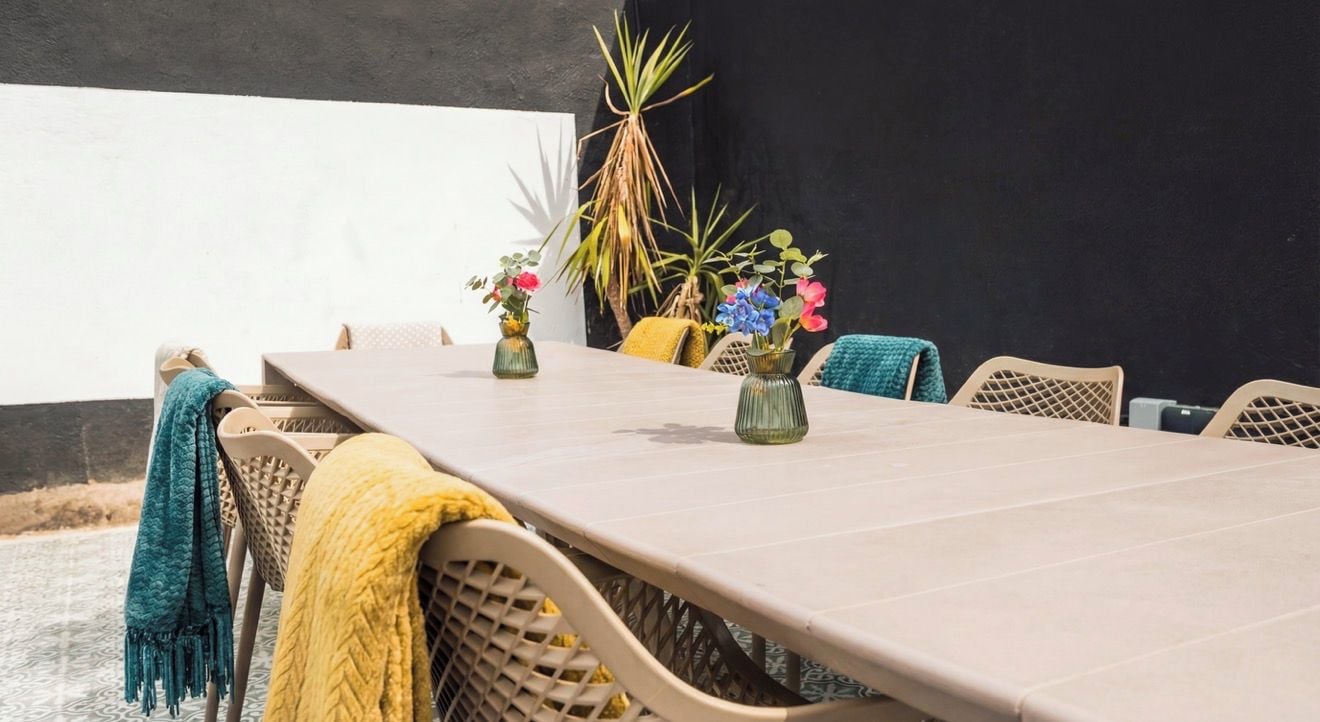 Una mesa de comedor con sillas, jarrones con flores y una pared negra al fondo.