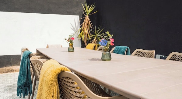 A dining table with chairs, vases with flowers, and a black wall in the background.