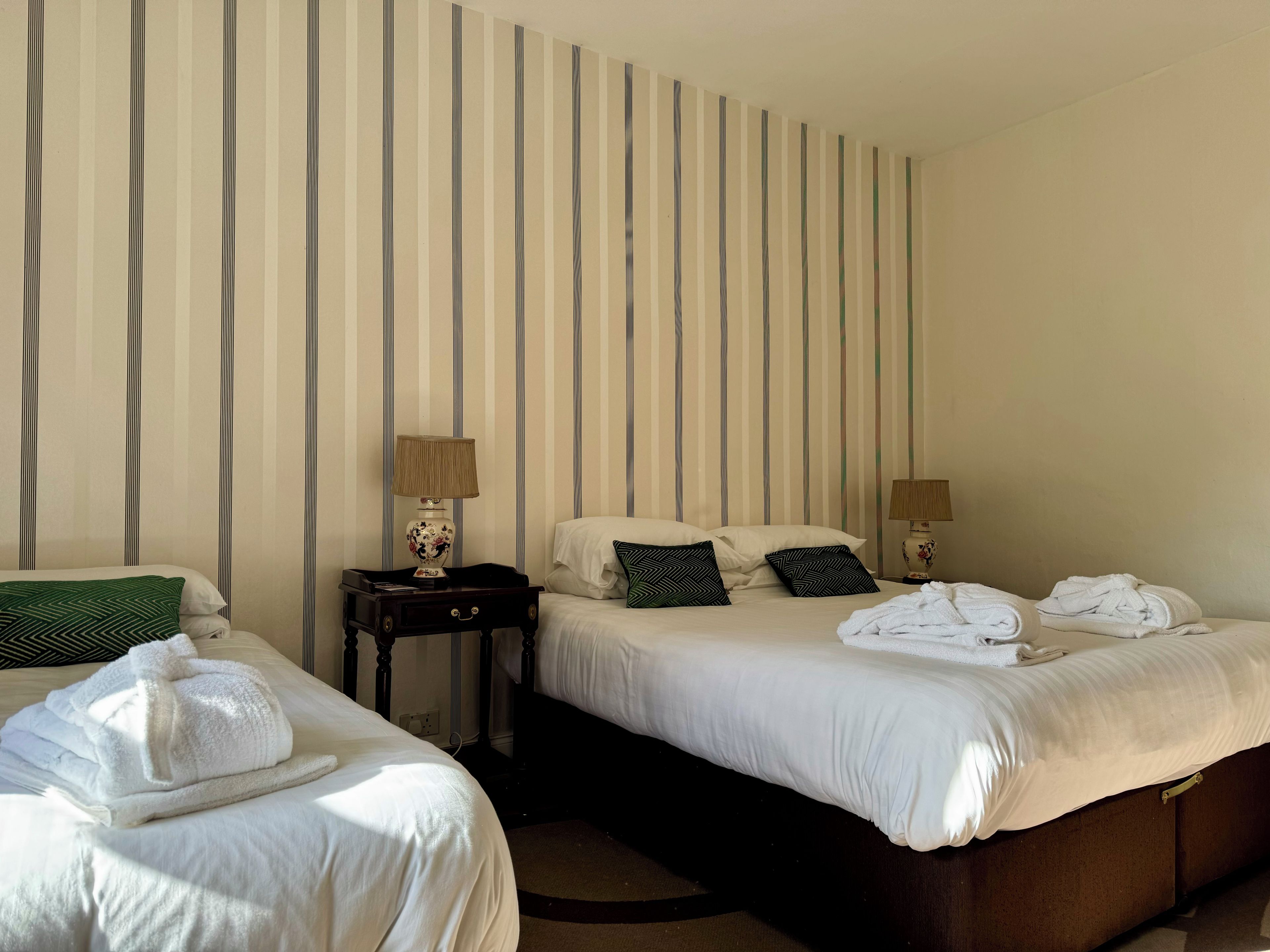 A hotel room with two beds, striped wallpaper, bedside lamps, and neatly folded towels.