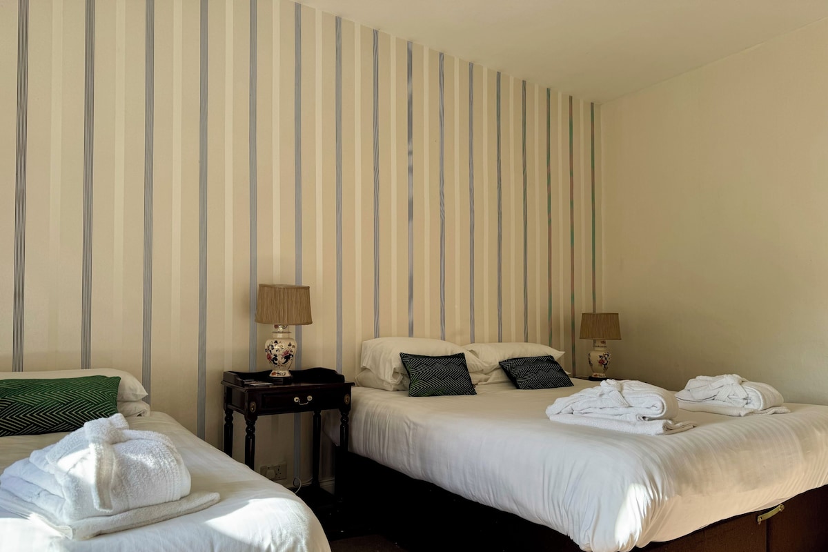 Une chambre d’hôtel avec deux lits, un papier peint à rayures, des lampes de chevet et des serviettes soigneusement pliées.