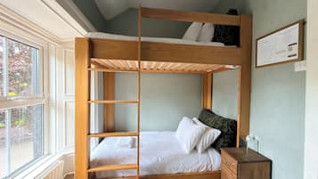 A bunk bed with a wooden frame, a bedside table, a radiator, and a window with a view of trees.