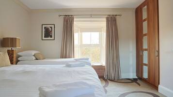 Habitación de hotel con una cama grande, una mesita de noche con lámpara, una ventana con cortinas y una puerta.