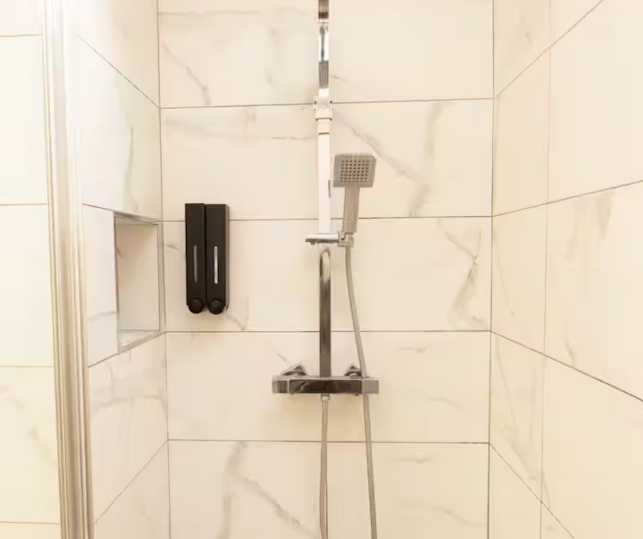 A shower area with a handheld showerhead and a wall-mounted control panel.