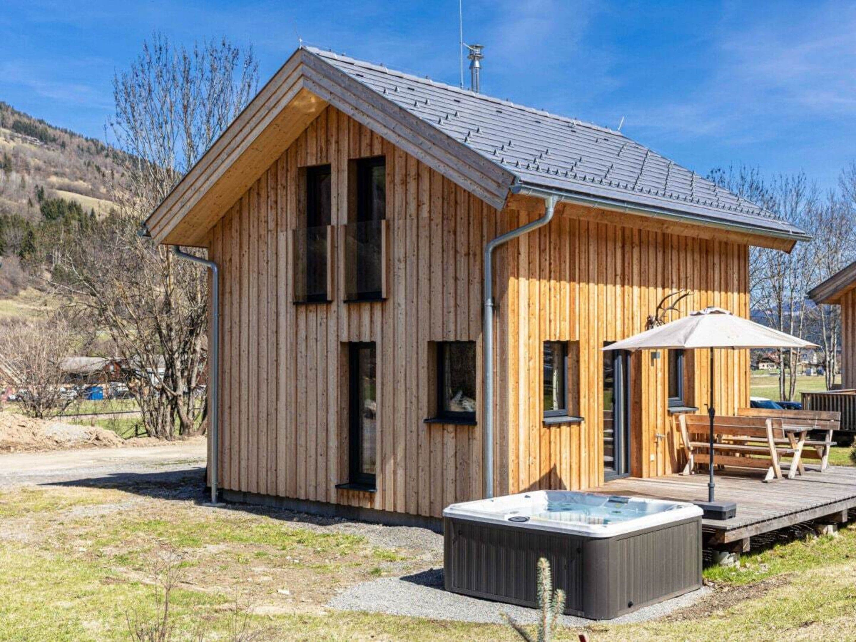 A wooden cabin with a hot tub, deck, and a view of the surrounding landscape.
