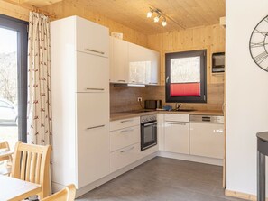 A modern kitchen with white cabinets, a built-in oven, and a window with red blinds. - One-bedroom Cabin (Sankt Georgen am Kreischberg)