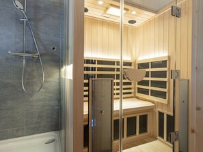 A sauna with a glass enclosure, wooden benches, and a shower area. - One-bedroom Cabin (Sankt Georgen am Kreischberg)